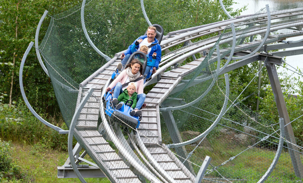 Familie fährt hintereinander mit dem Alpine Coaster am Ochsenkopf durch Kurven.