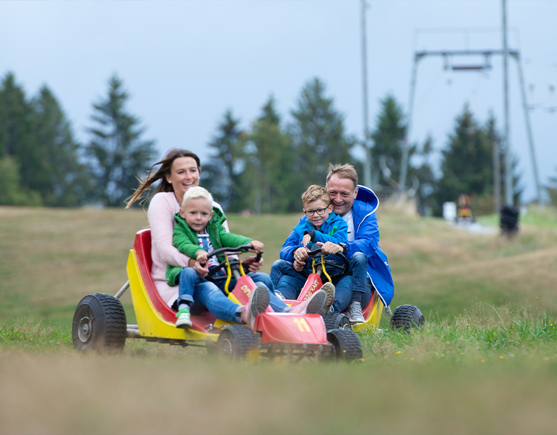 Familie düst mit Devalkarts bei Warmensteinach auf der Piste im Sommer bergab.