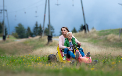 Mutter und Kind fahren mit einem Devalkart bergab über eine Wiese in Warmensteinach