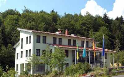 Gebäude der Tourist Information Fichtelberg mit Fahnen vor bewaldetem Hang.
