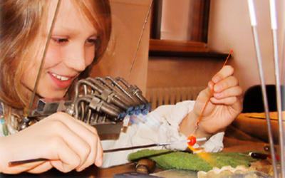 Kind fertigt in einer Glaswerkstatt eine Perle mit Brenner und Werkzeug.