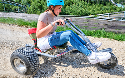 Frau fährt mit einem Mountaincart auf einer Schotterstrecke bergab.