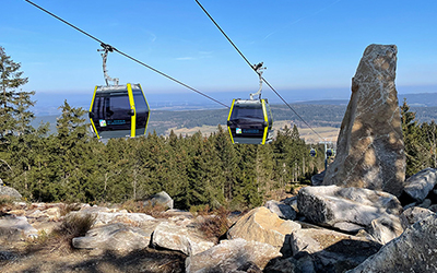 Gondeln der Seilbahn Ochsenkopf fahren über Felsen und Waldlandschaft.