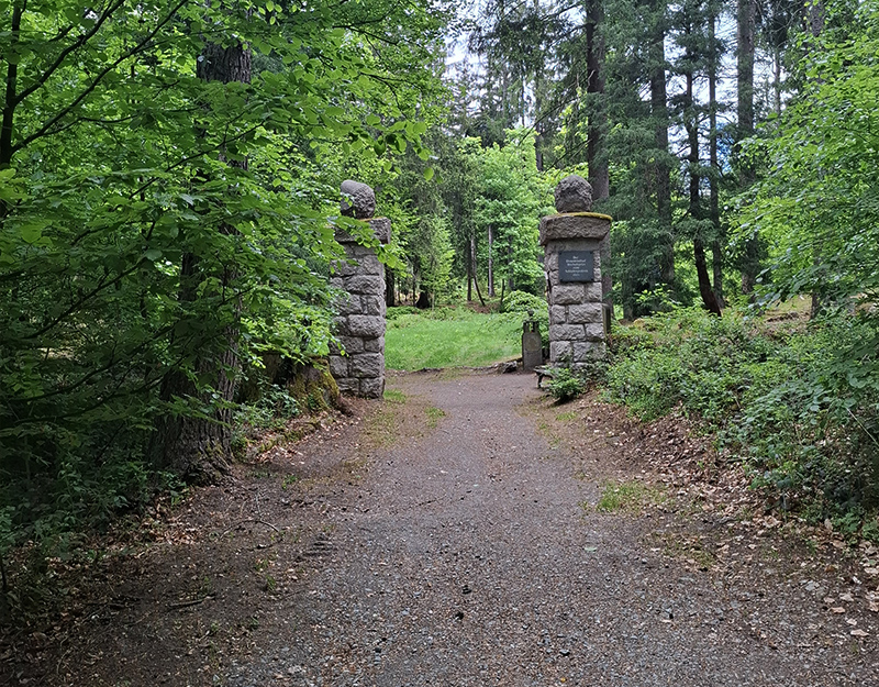 Eingangstor des Ehrenfriedhofs Bischofsgrün mit steinernen Säulen im Wald.