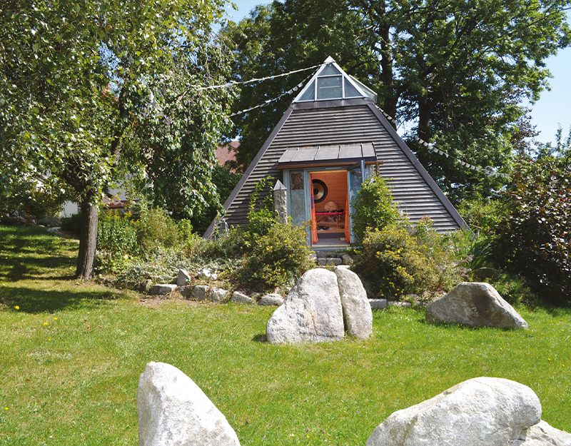 Außenansicht einer Klangpyramide inmitten eines Gartens.