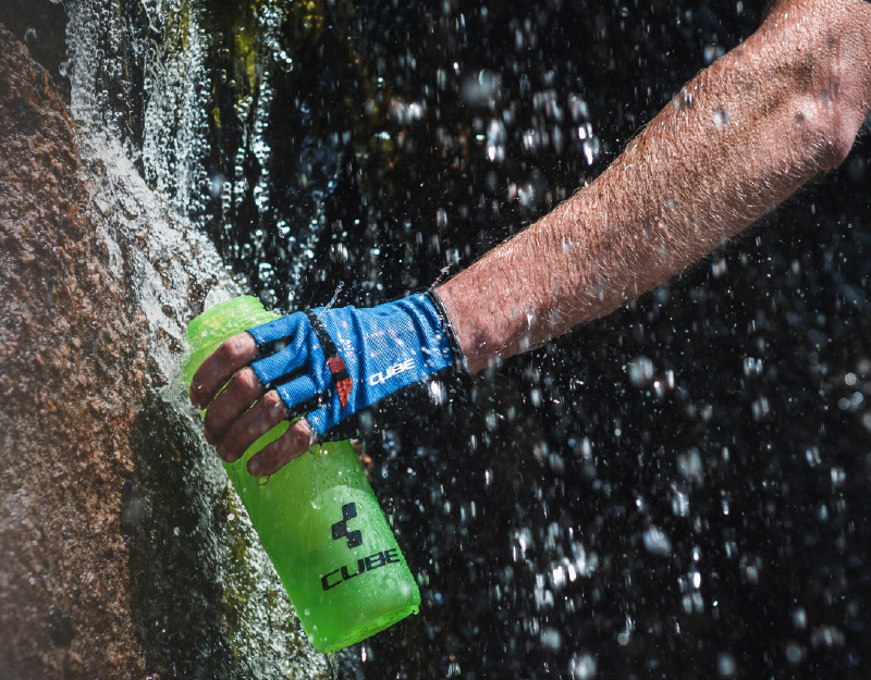 Mann füllt Trinkflasche mit Wasser am Bach wieder auf.