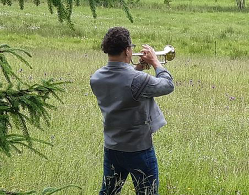 Mann spielt Trompete auf einer Wiese entlang des Echowaldwegs.