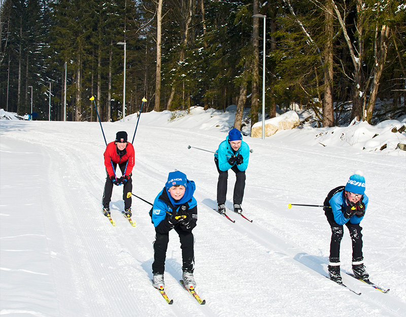 Vier Langläufer fahren in gebückter Haltung auf der Loipe an der Bleaml Alm im klassische Stil entlang.