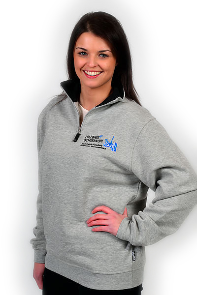 Frau präsentiert grauen Pullover mit Logo der Erlebnisregion Ochsenkopf vor neutralem Hintergrund.