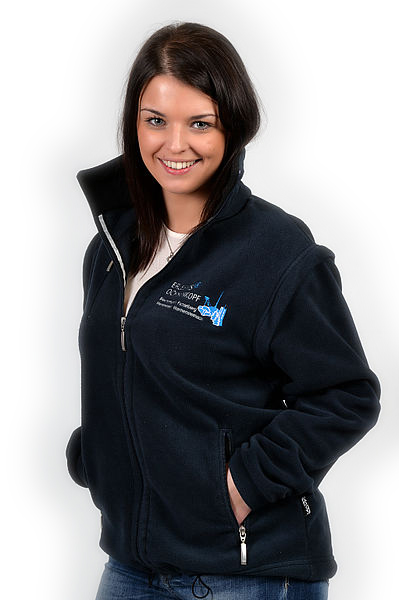 Frau trägt dunkelblaue Fleecejacke mit gesticktem Erlebnis-Ochsenkopf-Logo.