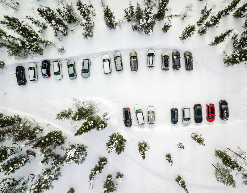 Luftaufnahme eines verschneiten Parkplatzes im Fichtelgebirge mit parkenden Autos zwischen winterlichen Bäumen.