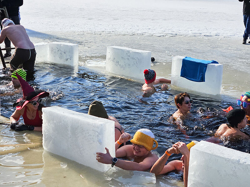 Mehrere Badegäste baden bei eisiger Kälte im zugefrohreren Fichtelsee in Fichtelberg.