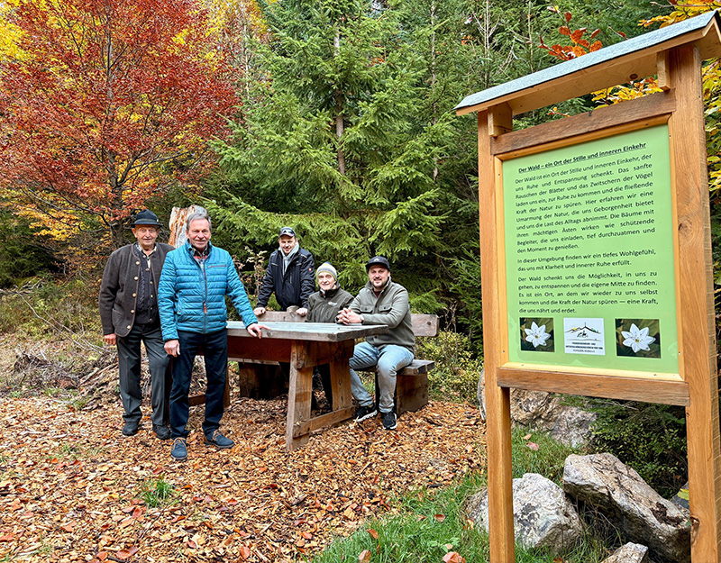 Gruppe von Wanderern an einer Sitzgruppe mit Infotafel „Ort der Stille“ im herbstlichen Wald bei Fichtelberg.